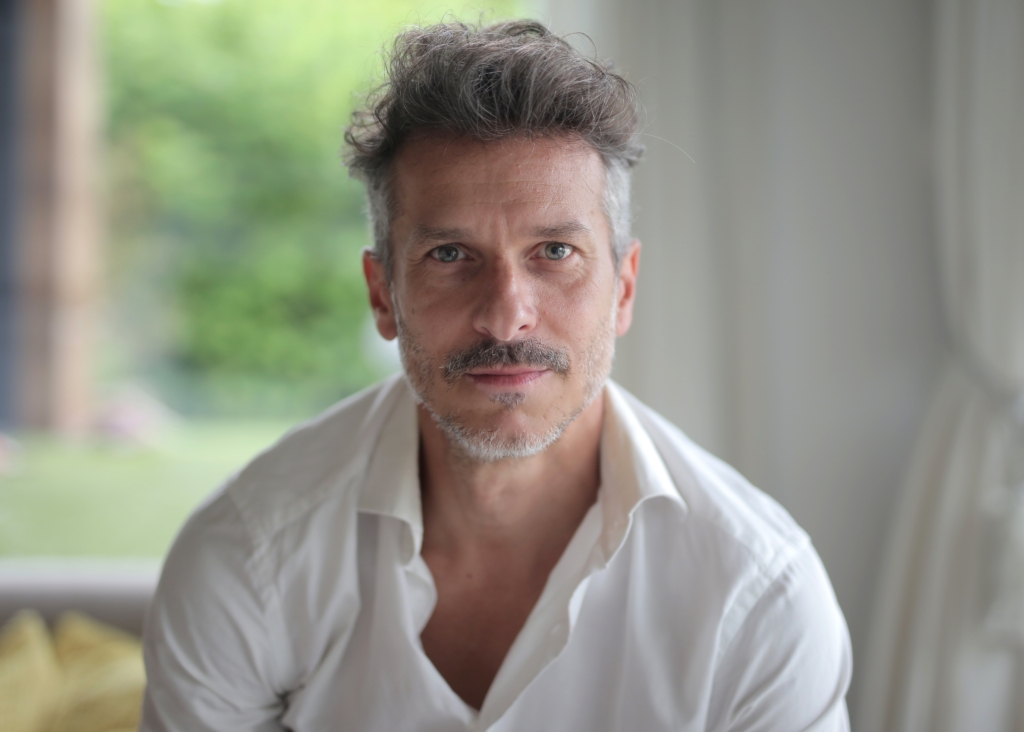 Portrait of an adult male with a quiff and blue eyes under the lights with a blurry background